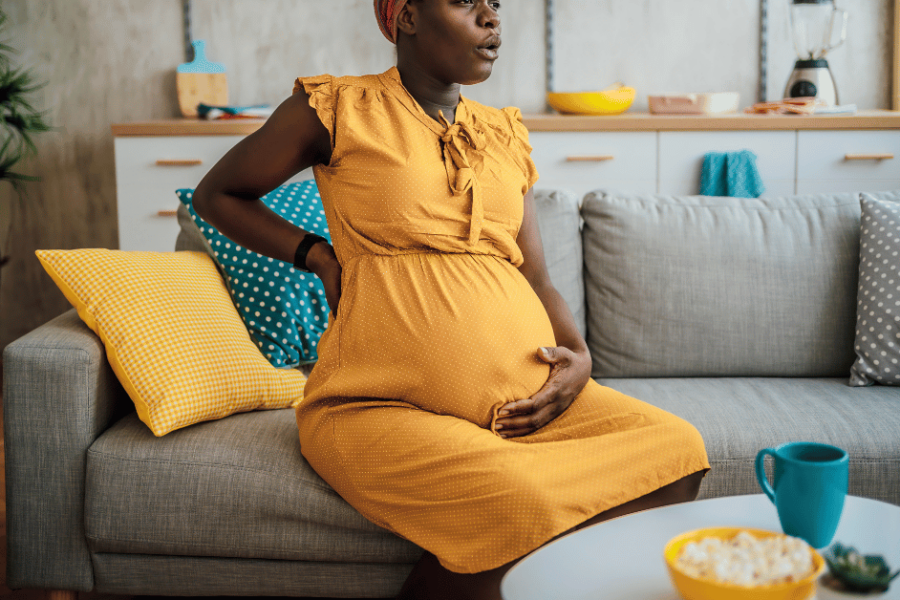 A pregnant woman in discomfort sits on a couch.
