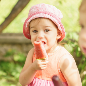 A young girl eats a fruit popsicle.