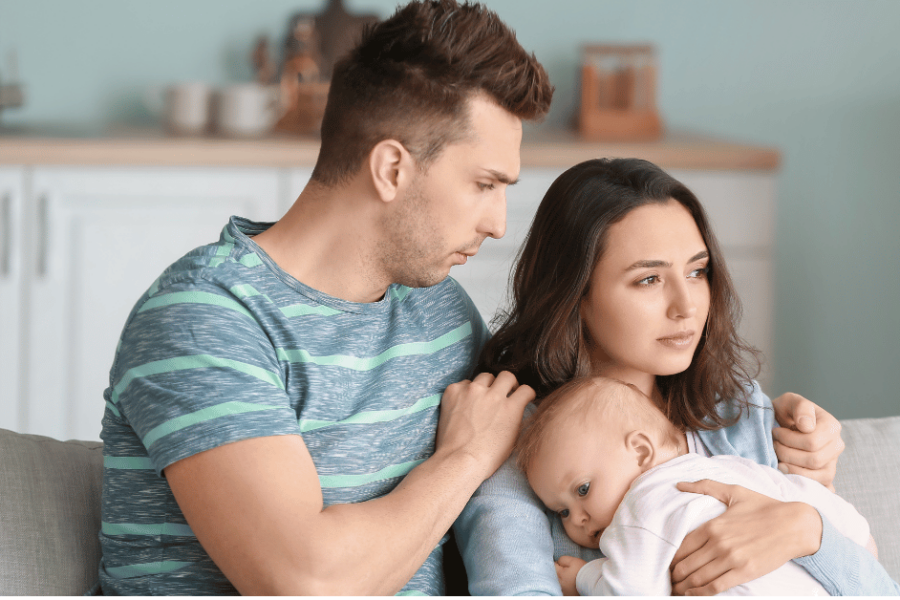 Stressed parents hold their infant while sitting on a couch.