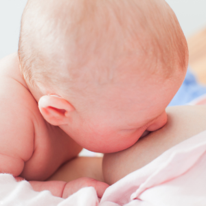 An undressed baby breastfeeds while laying on the mother's bare chest.