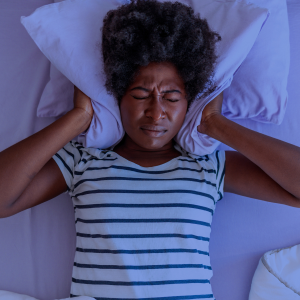 A woman holds a pillow over her ears as she tries to sleep. 