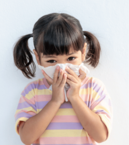 A young girl wearing a striped shirt blows her nose.