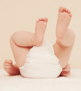 A baby wearing a diaper lays on a white blanket.