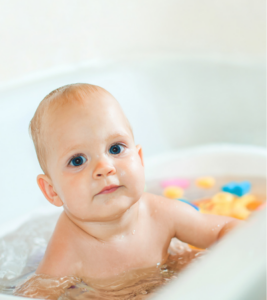 A young toddler sits in a bath. 