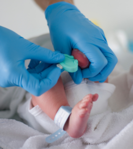 A medical professional performs a heel stick test on a newborn.