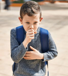 A boy is coughing while walking home from school.