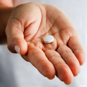 A woman's hand holding an aspirin. 