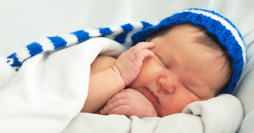 A newborn baby with mild jaundice wearing a blue cap.