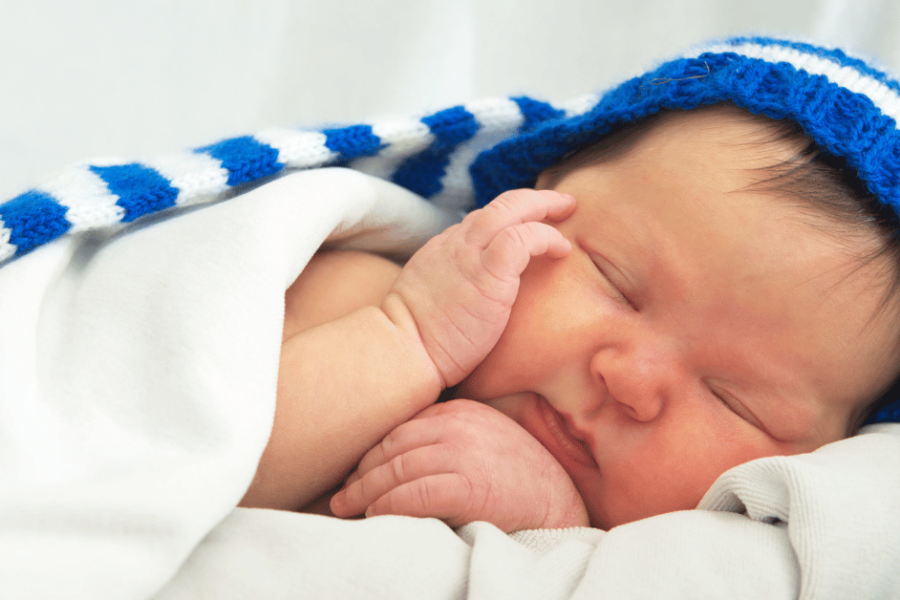 A newborn baby with mild jaundice wearing a blue cap.