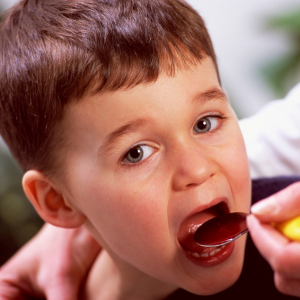 A boy swallows a spoonful of medicine.