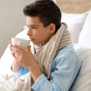 A boy sick in bed drinks broth from a mug.