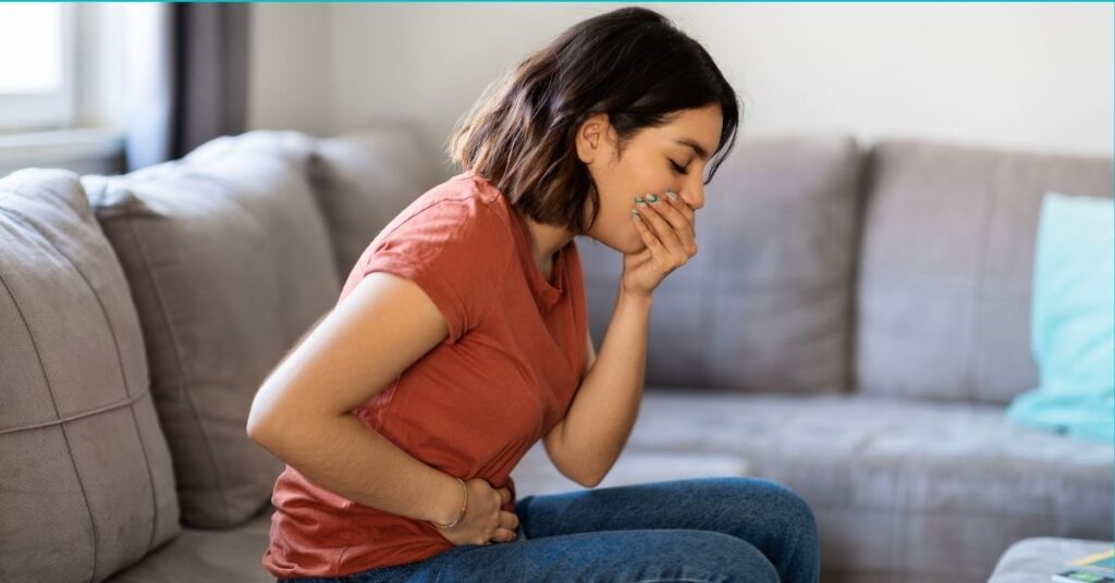 An ill woman places hands over her stomach and mouth.