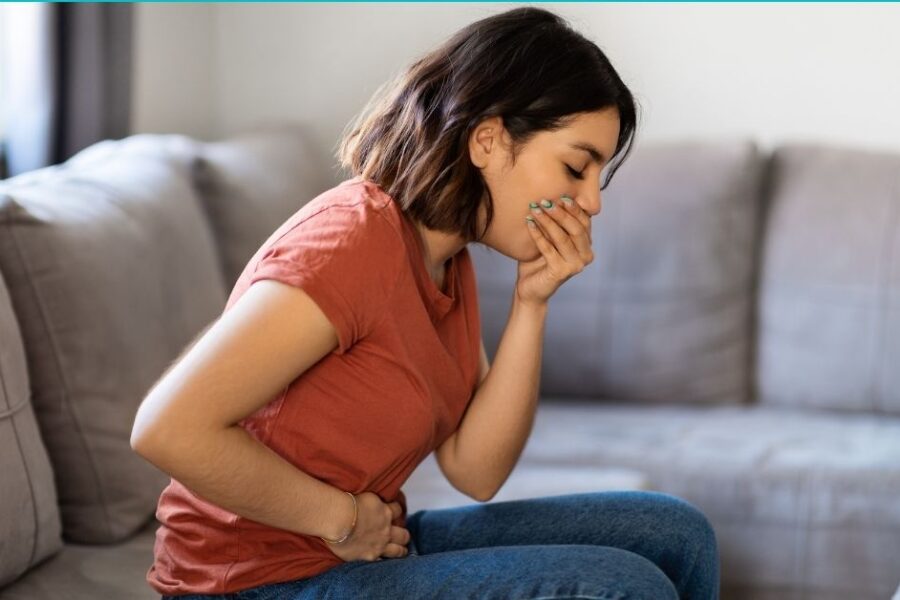 An ill woman places hands over her stomach and mouth.