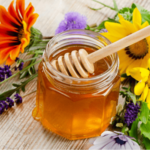 A glass jar of honey surrounded by flowers.