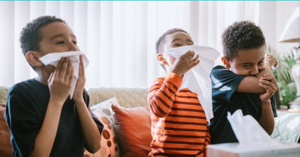 Three boys sitting on a couch blowing their noses.