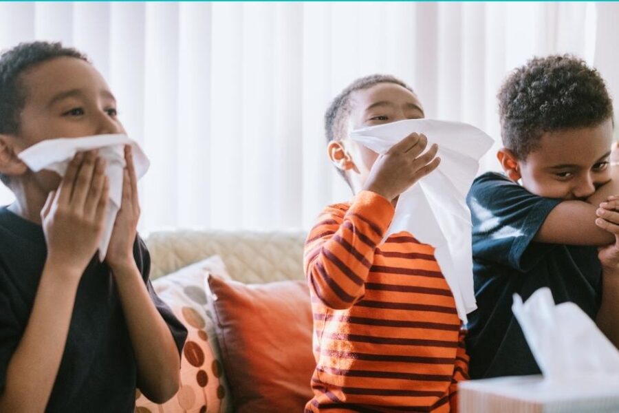 Three boys sitting on a couch blowing their noses.