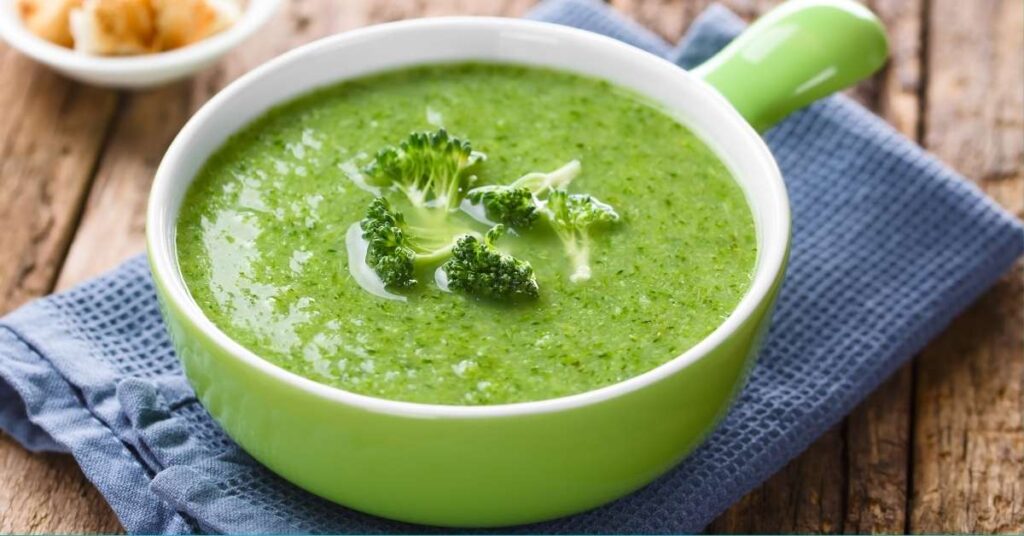 A bowl of broccoli soup next to a blue dish towel.