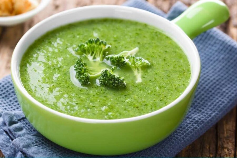 A bowl of broccoli soup next to a blue dish towel.