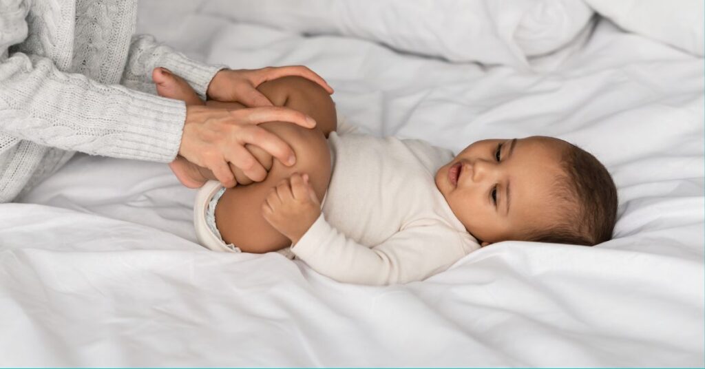 A mom gently presses her baby's legs into their stomach to help relieve constipation.