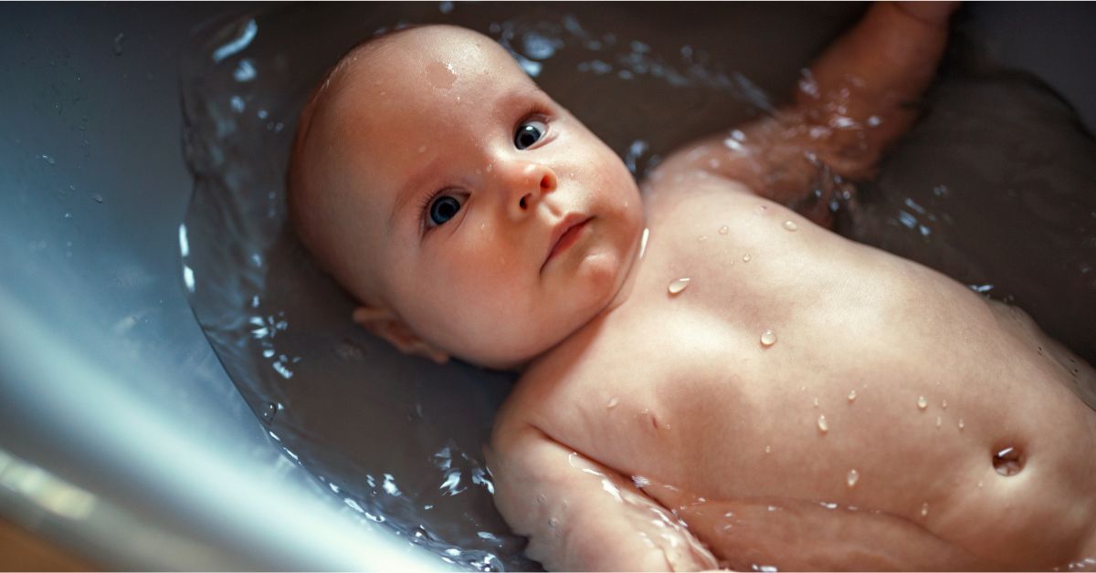 A baby lays calmly in water in a baby bath tub.