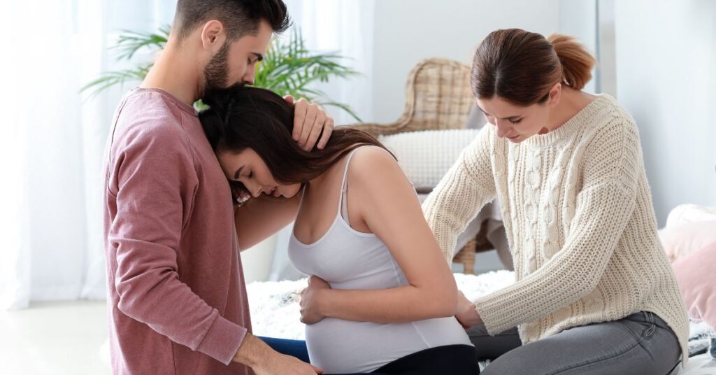 A pregnant woman is supported by her husband and midwife.
