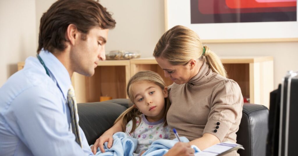 A doctor takes notes while visiting with a sick child and her parent.