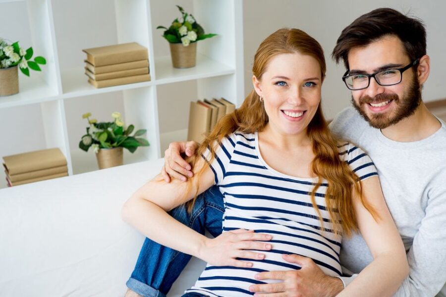 A pregnant woman and her husband sit on a couch.