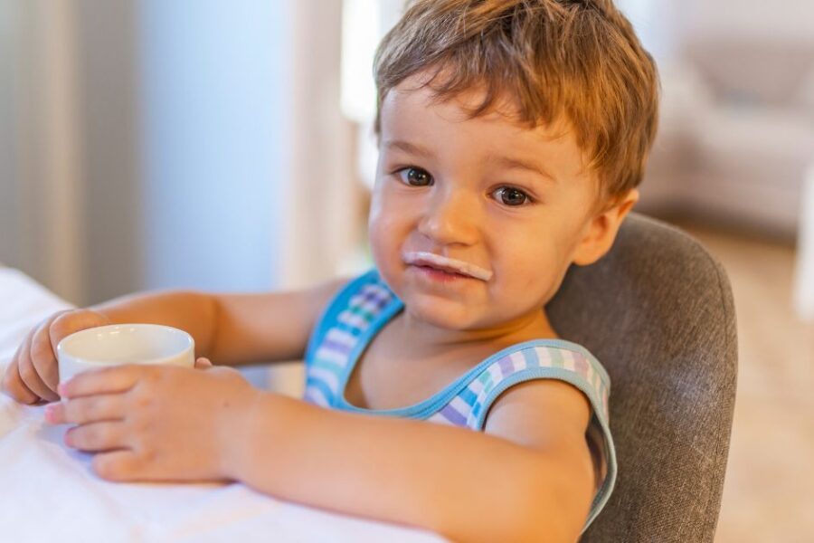 A toddler drinks milk from a small cup while sitting at a table.