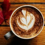 A cup of coffee with cream on a wooden counter.