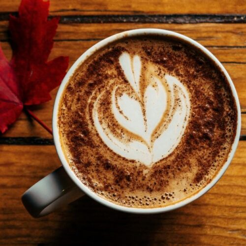 A cup of coffee with cream on a wooden counter.