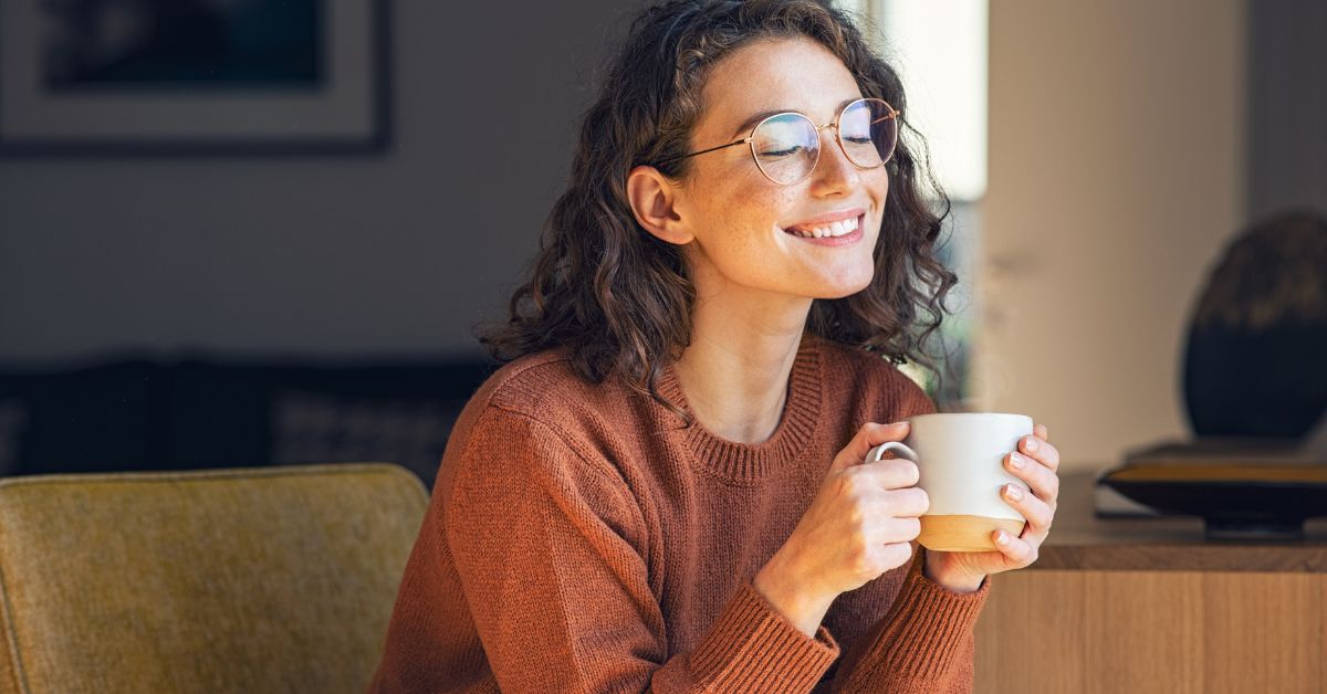 A woman smiles while holding a cup of coffee.