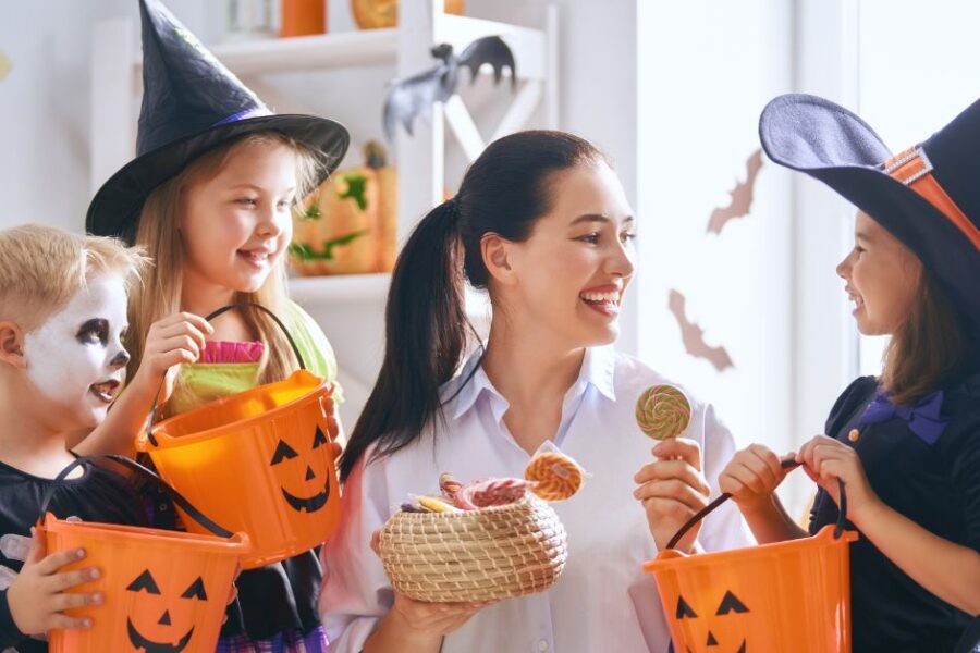 A woman hands candy to children dressed in Halloween costumes.