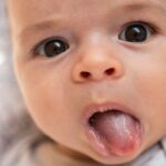 An infant sticks his tongue out.