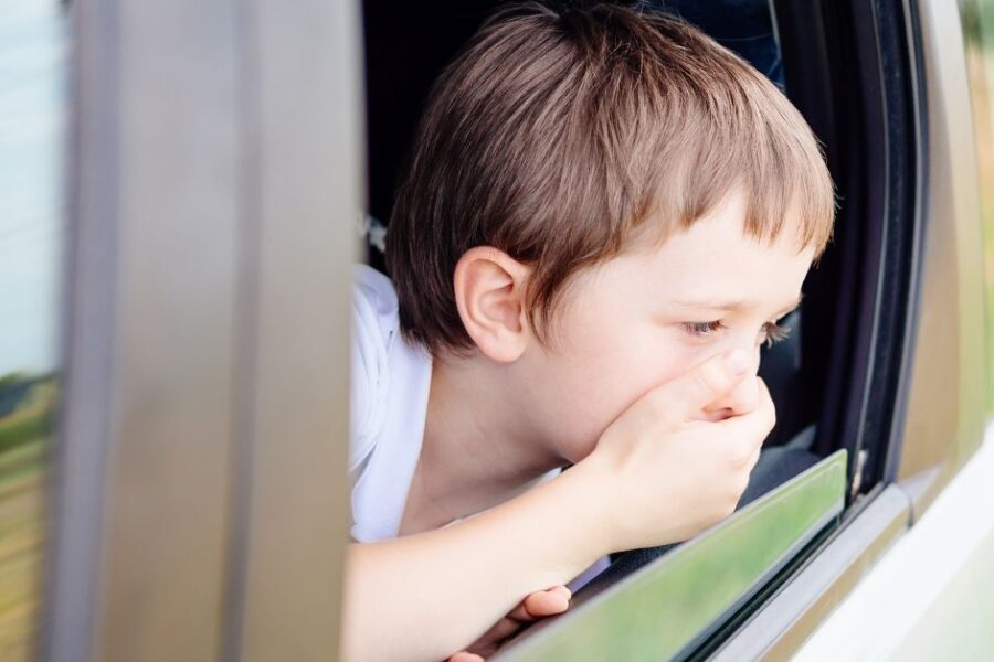 A sick boy sticks his head out of a car window.