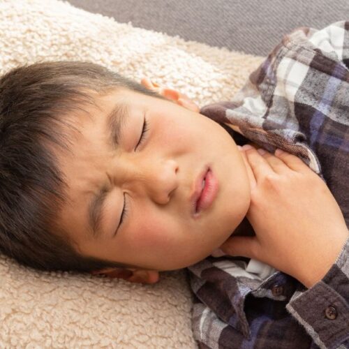 A boy with a sore throat places his hand on his neck.