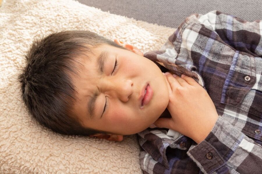 A boy with a sore throat places his hand on his neck.
