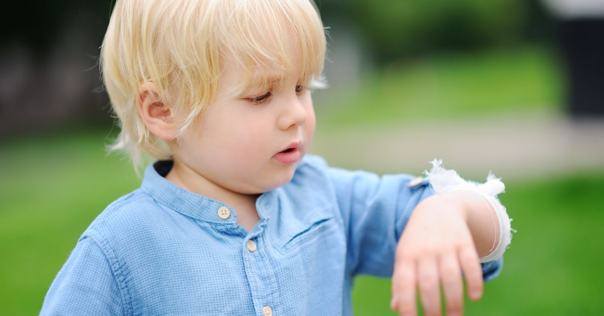 A toddler holds up his sore arm.