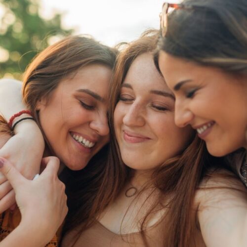 Three teenage girls hug each other.