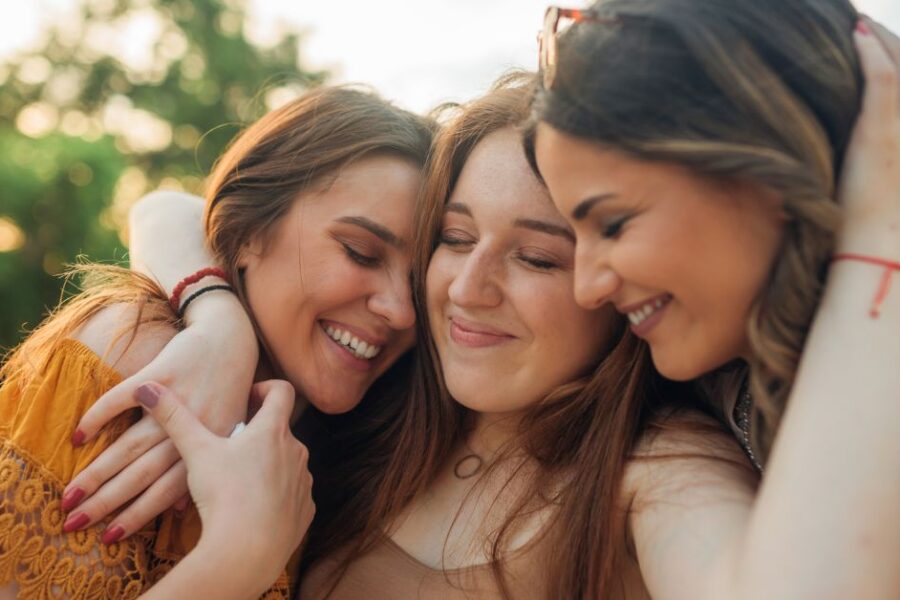 Three teenage girls hug each other.