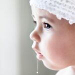 A baby girl has drool hanging from her mouth.