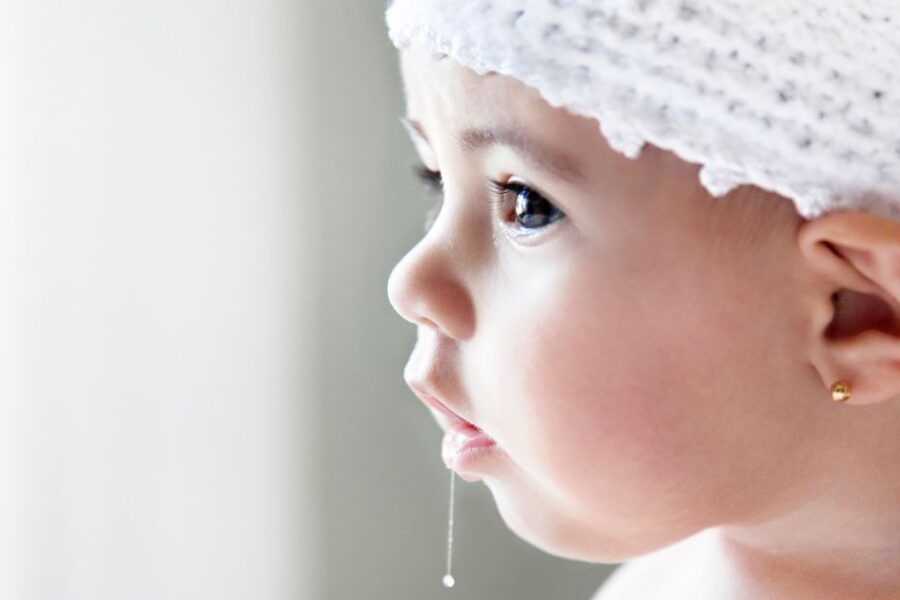A baby girl has drool hanging from her mouth.