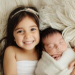 Two young girls lay next to each other on a sheep skin rug.