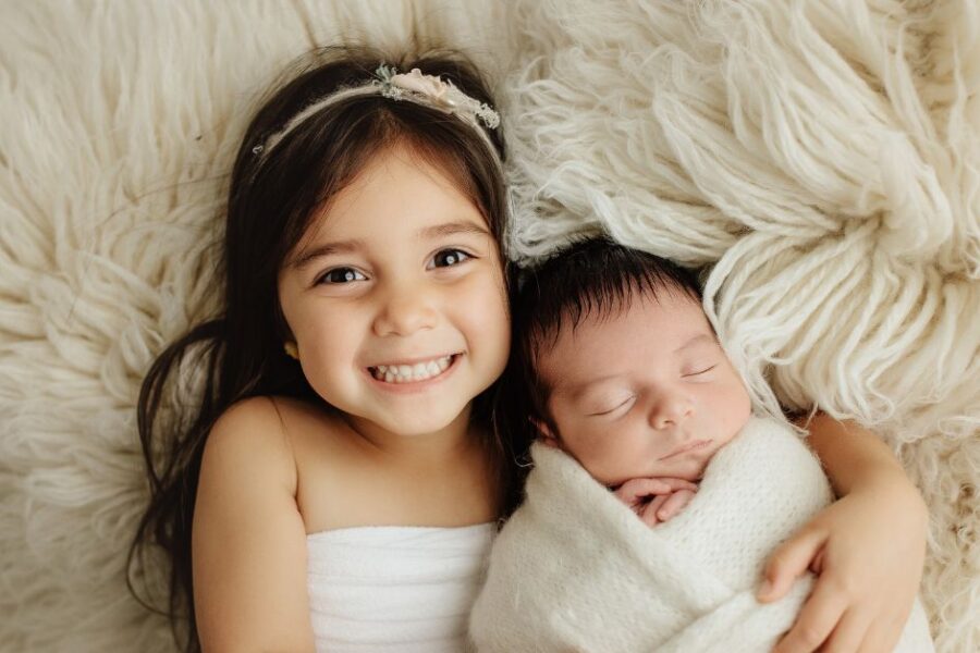 Two young girls lay next to each other on a sheep skin rug.