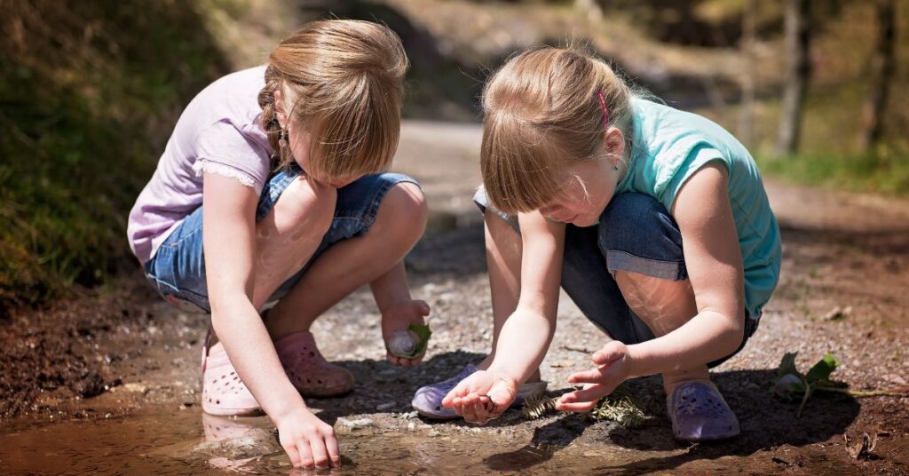 Two girls play in the dirt near a stream.