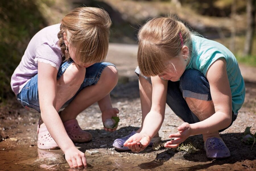 Two girls play in the dirt near a stream.