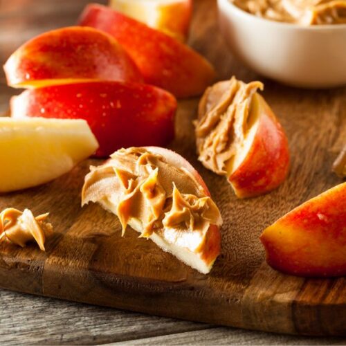 Apple slices with dabs of peanut butter on a wooden cutting board.