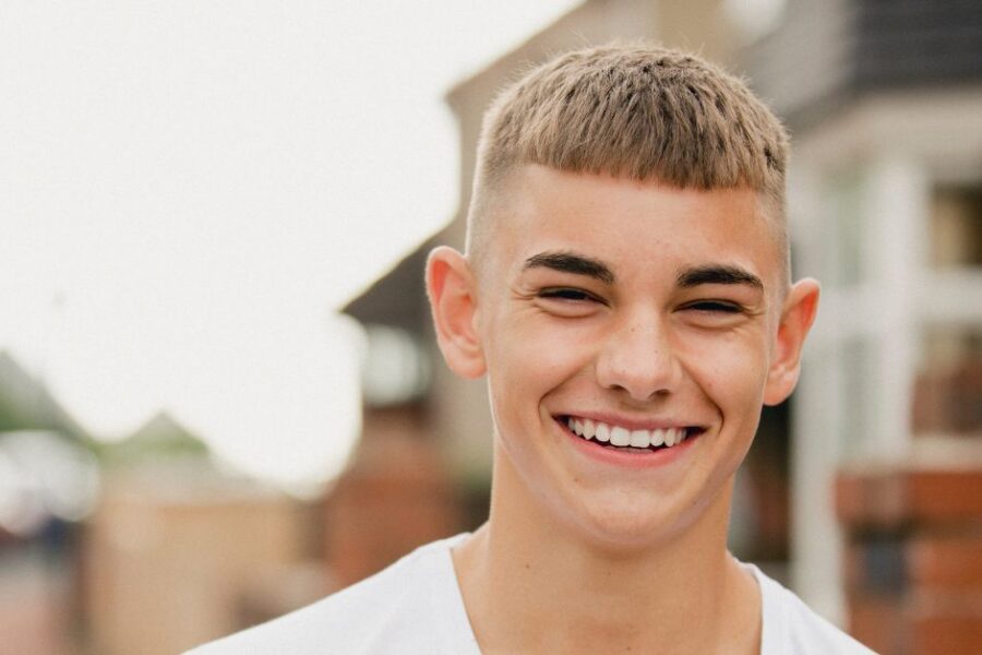 A teenage boy smiles while walking outdoors.