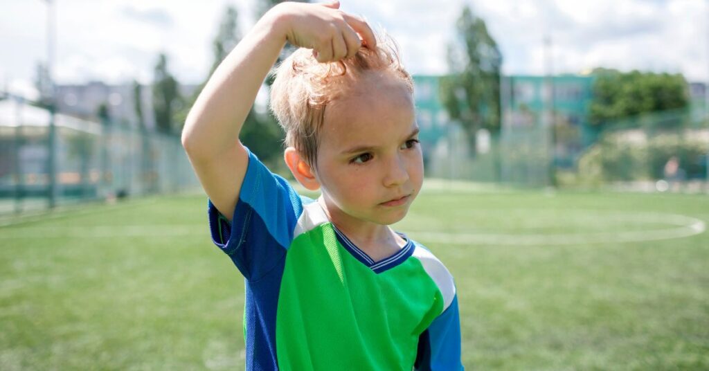 A boy playing outside pushes his sweaty hair off of his forehead.