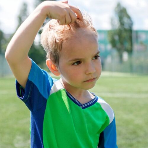 A boy playing outside pushes his sweaty hair off of his forehead.