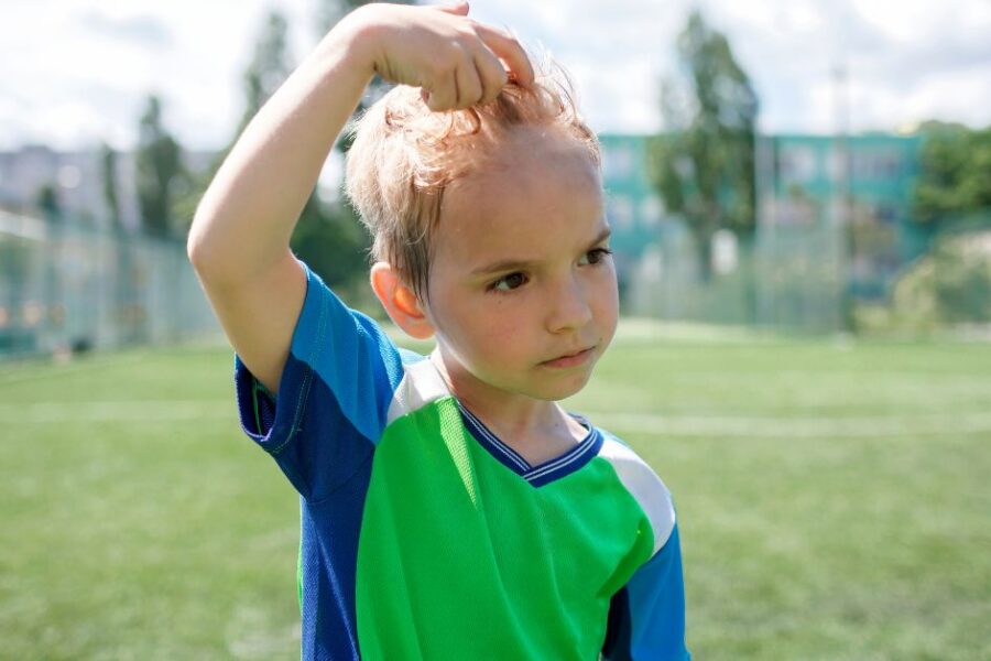 A boy playing outside pushes his sweaty hair off of his forehead.